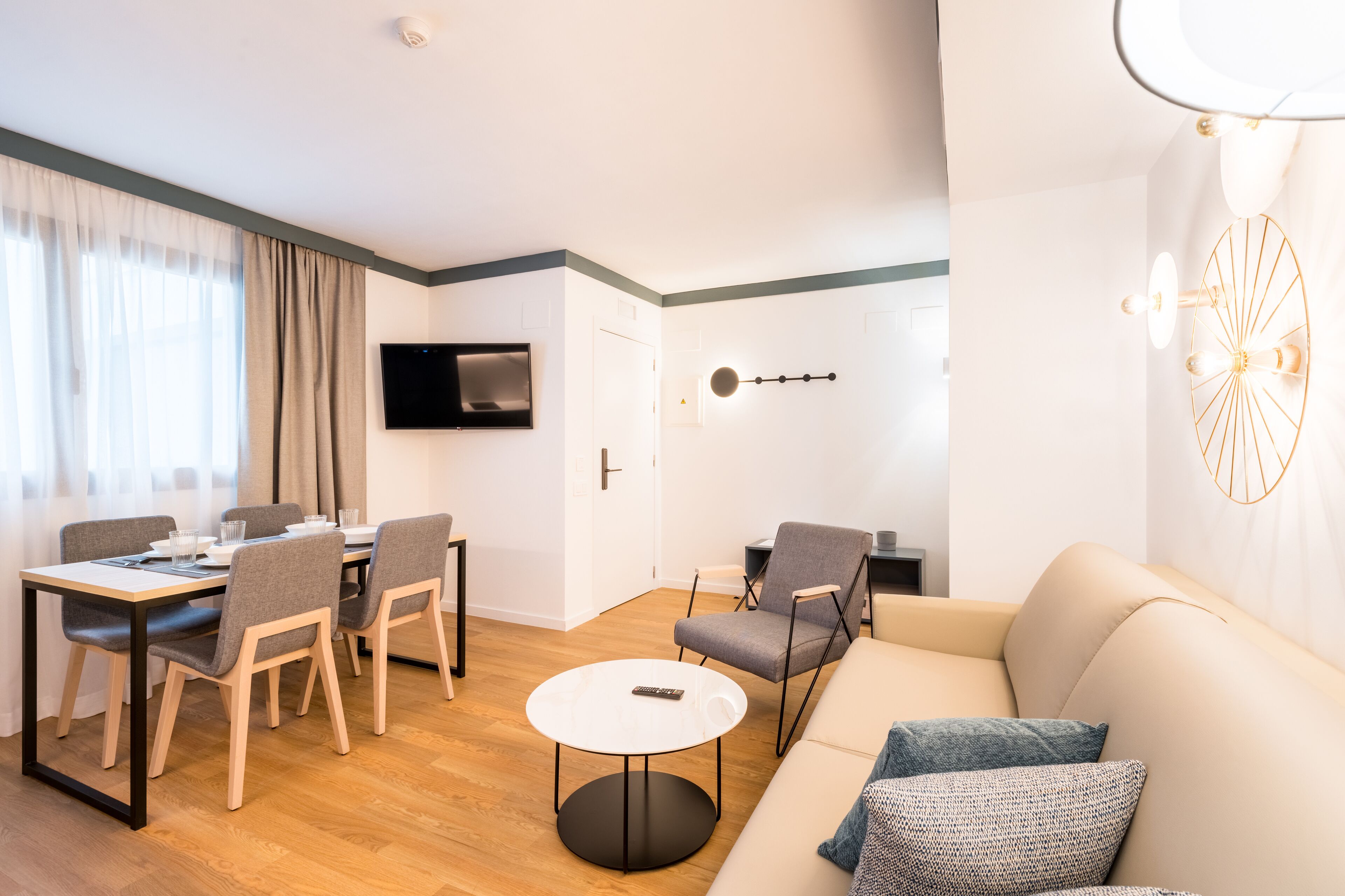 Ein modernes Wohnzimmer mit einer Couch, einem Esstisch mit Stühlen, einem an der Wand befestigten Fernseher und einer außergewöhnlichen Wandleuchte.