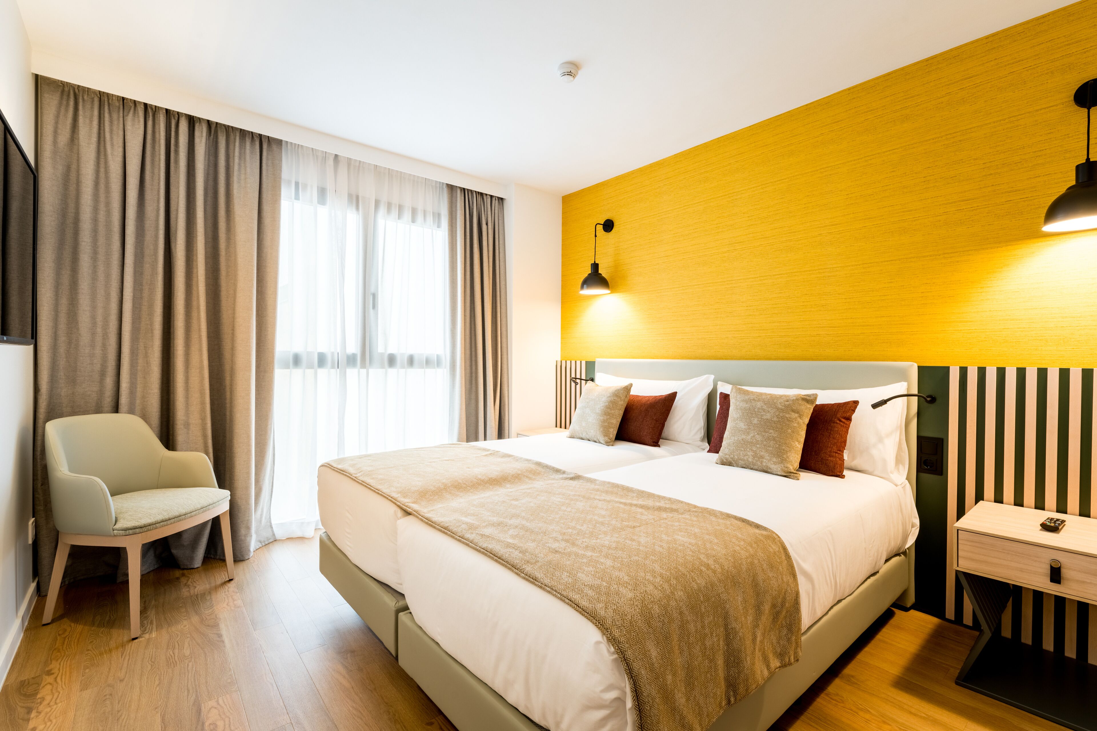 A hotel room with a large bed, a bedside table, a chair, and a window with curtains.
