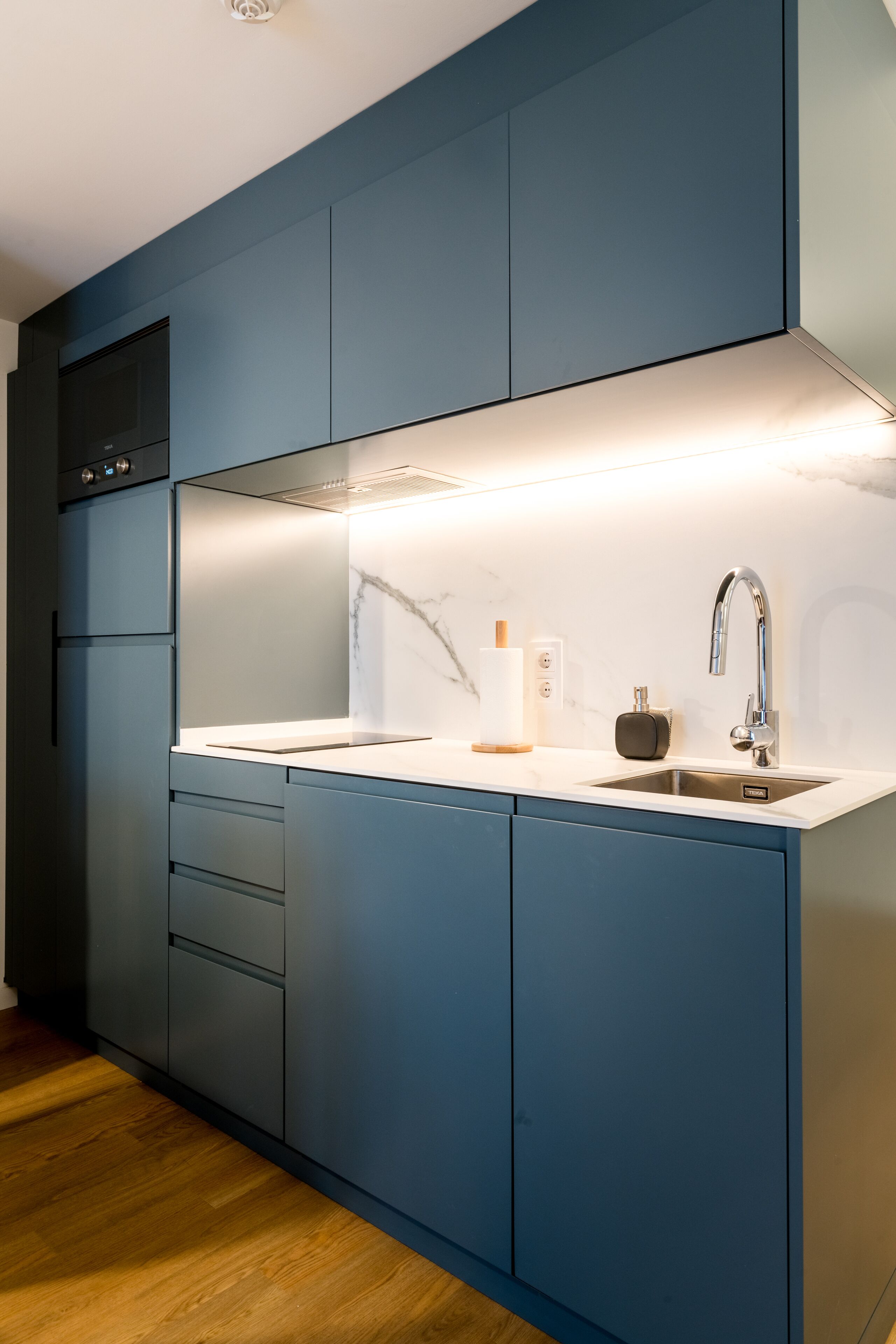 A modern kitchen with dark blue cabinets, a white countertop, and a stainless steel sink.