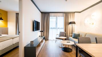 A modern hotel room with a bed, a TV, a sofa, a dining table, and a lamp.
