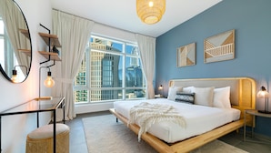 Ein modernes Schlafzimmer mit einem großen Bett, einem Nachttisch, einem Spiegel und Blick auf die Stadt durch große Fenster.