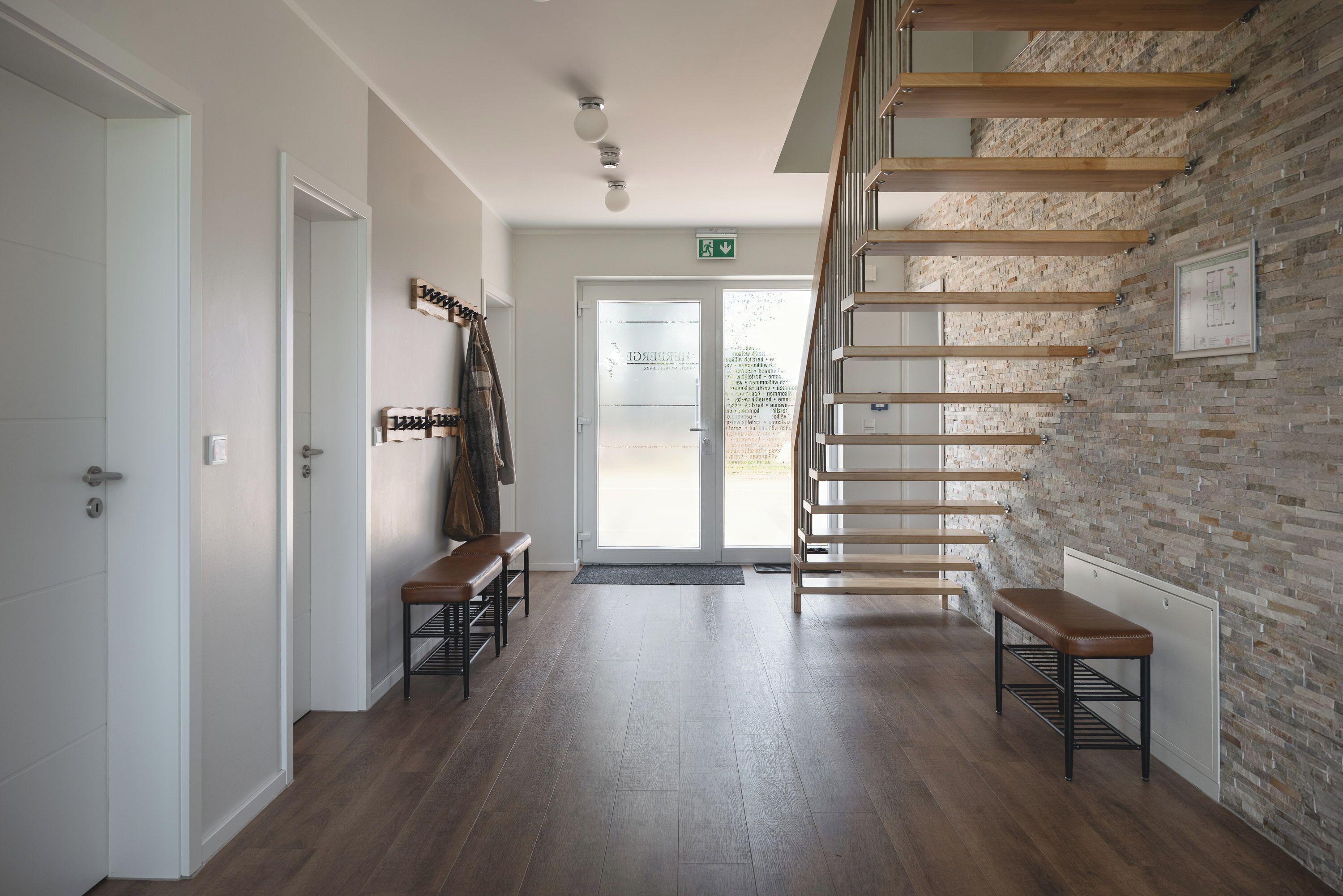 Ein Flur mit einer Holztreppe, Bänken und einer Tür mit Kleiderhaken.