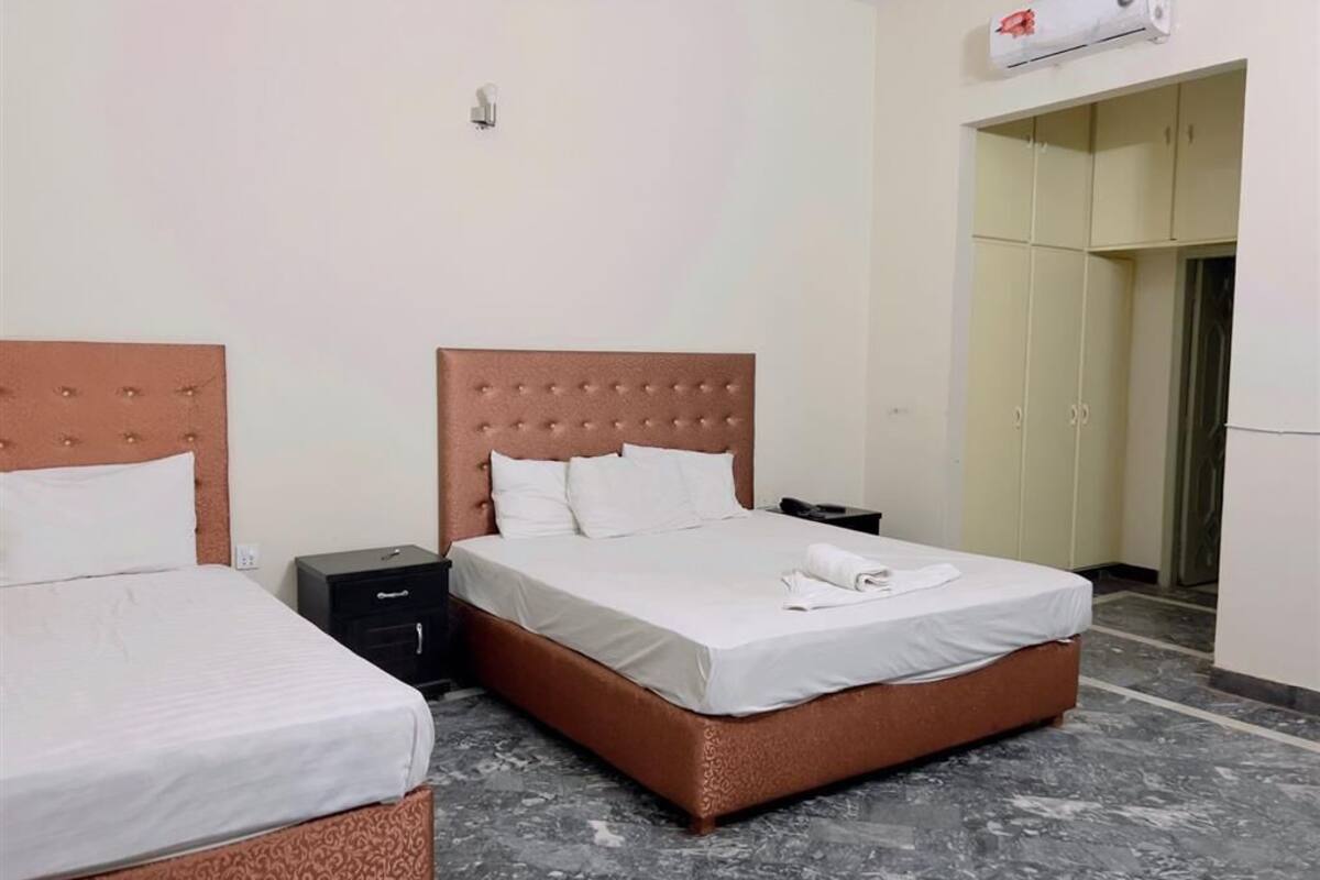A hotel room with two beds, a marble floor, a wardrobe, and a ceiling-mounted air conditioning unit.