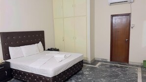A bedroom with a bed, a wardrobe, a door, and an air conditioning unit. - Hotel Rose Inn (Lahore)