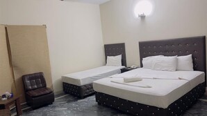 A hotel room with two beds, a small table, a chair, and a ceiling fan. - Hotel Rose Inn (Lahore)
