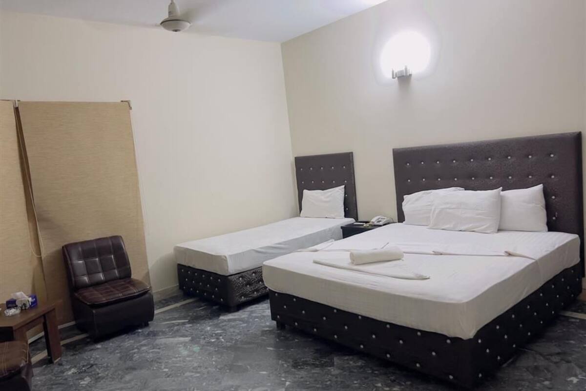A hotel room with two beds, a small table, a chair, and a ceiling fan.