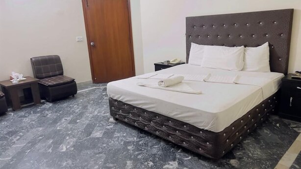 A neatly arranged bedroom with a large bed, a wooden door, a chair, and a small table. - Hotel Rose Inn (Lahore)