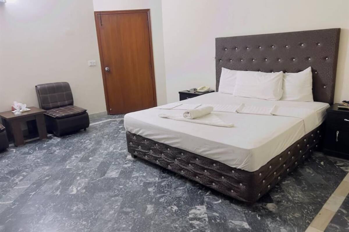 A neatly arranged bedroom with a large bed, a wooden door, a chair, and a small table.