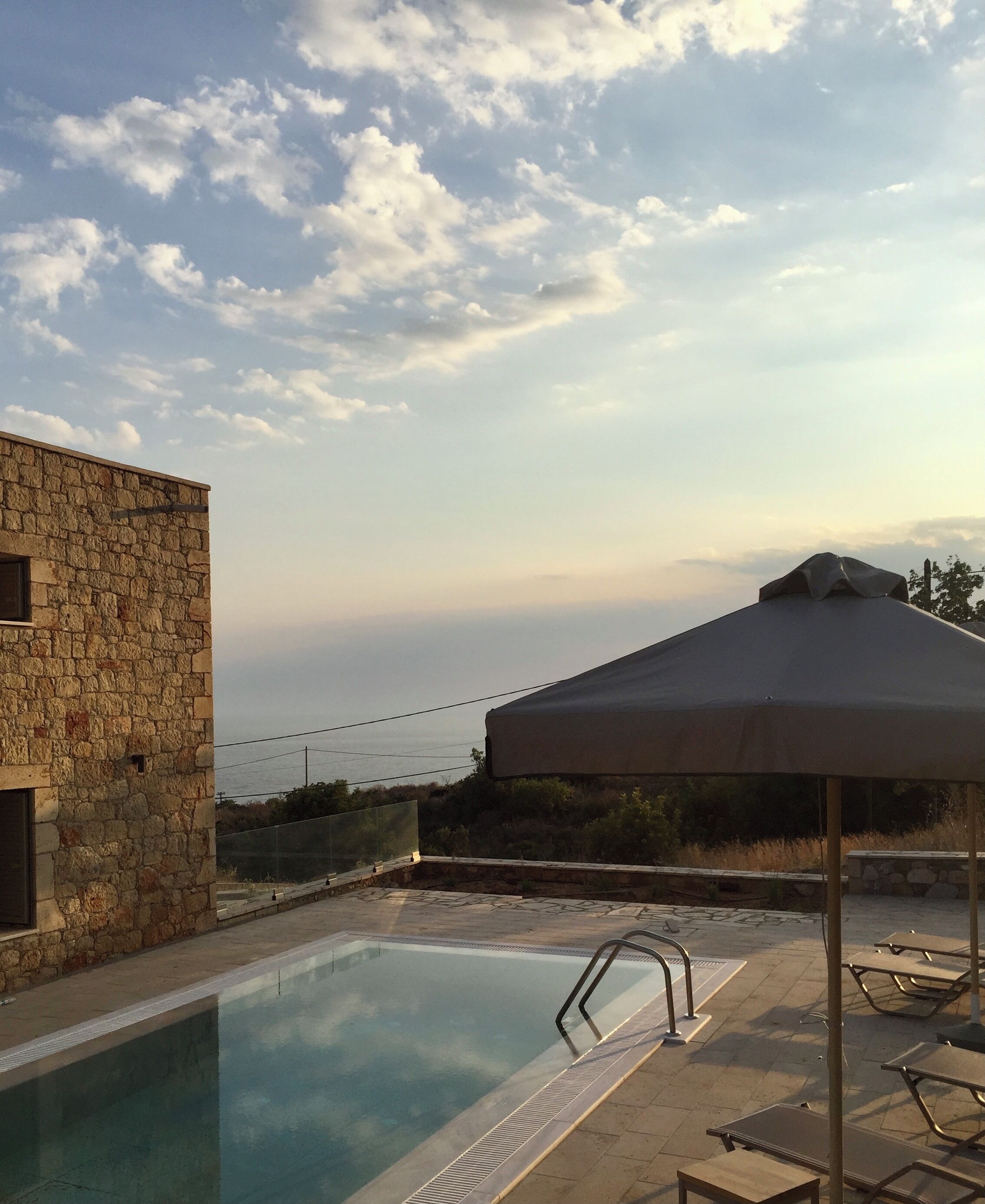 A pool area with a stone building, a covered seating area, and a view of the sea.