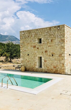 A stone building with a pool, surrounded by a mountainous landscape.