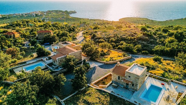 An aerial view of a coastal property with multiple swimming pools, stone buildings, and lush greenery.