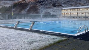 A swimming pool with diving boards, surrounded by a fenced area with a view of a building and hills in the background. - Dalahótel (Budardalur)