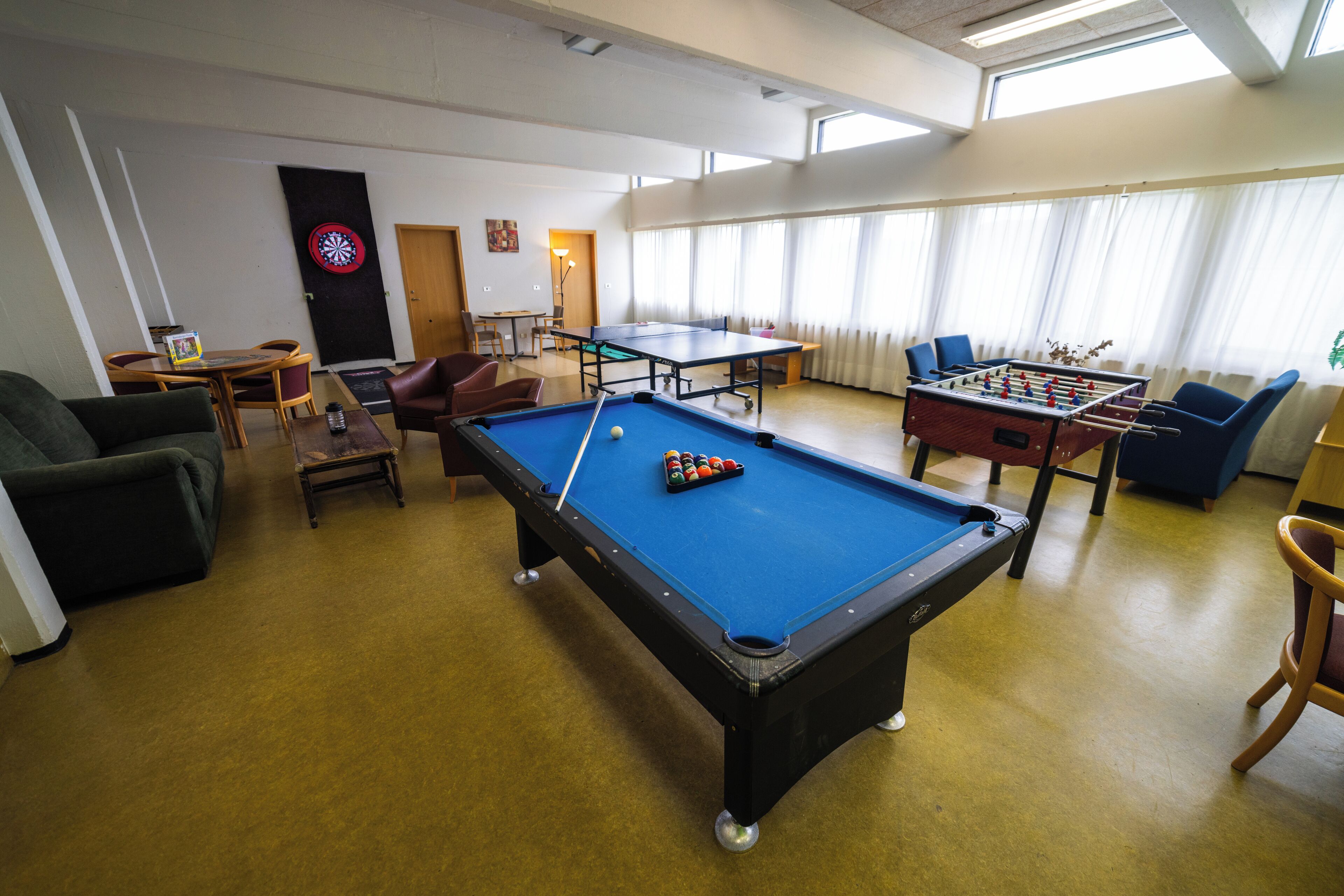 A recreational room with a pool table, foosball table, and dartboard.