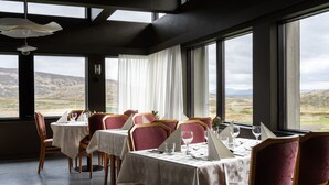 A dining area with tables set for four, large windows offering a view of the countryside, and a modern interior design with dark walls and wooden chairs. - Dalahótel (Budardalur)