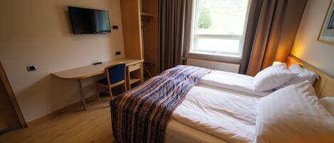 A hotel room with a bed, a desk, a chair, a television, and a window with curtains.