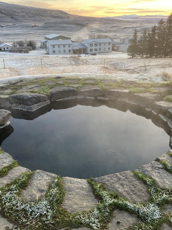 A clear view of a small pond surrounded by stone steps and grass, with a building in the background.