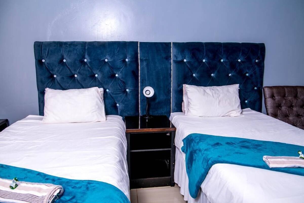 Een hotelkamer met twee bedden, een nachtkastje en een blauw hoofdeinde.