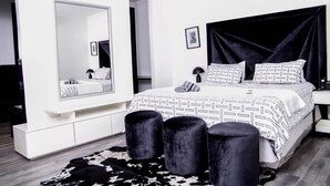 A modern bedroom with a large mirror, a black upholstered headboard, and a patterned bedspread. - ZAI OAT HOTEL (Makhuduthamaga)