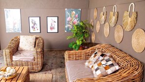 A room with wicker furniture, including two chairs and a sofa, a small table with a bowl of snacks, and a potted plant. - ZAI OAT HOTEL (Makhuduthamaga)
