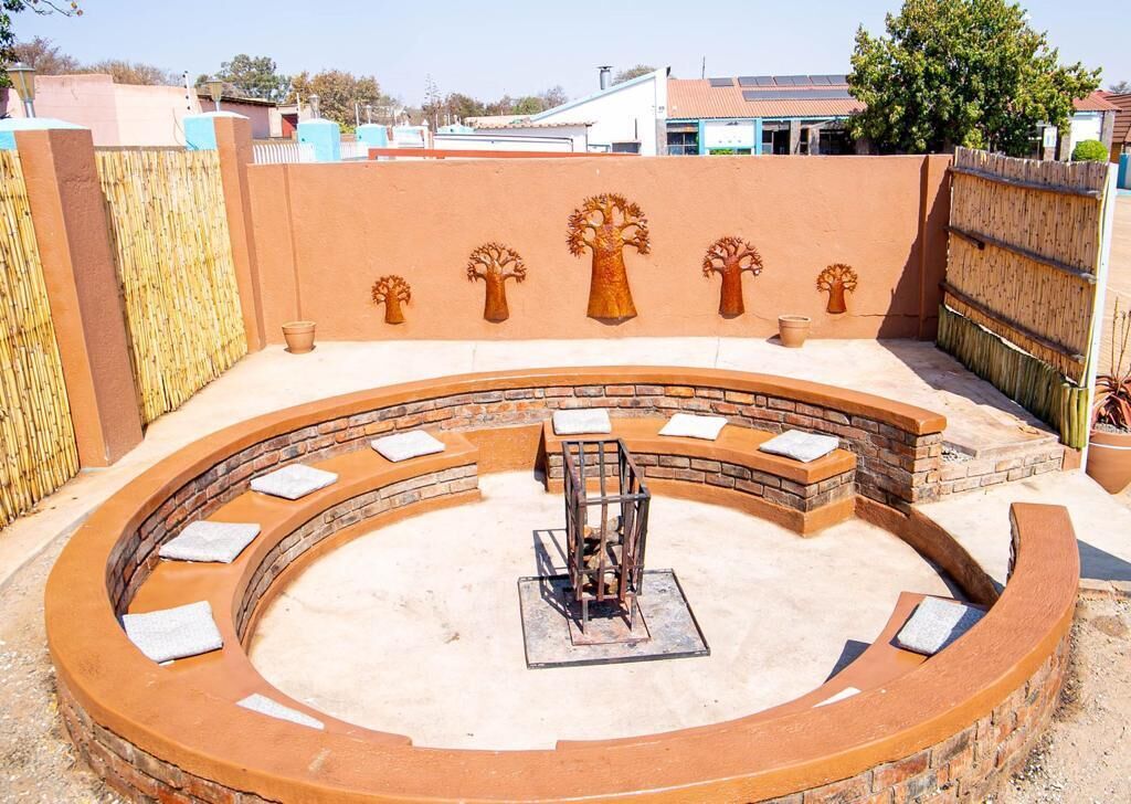 A circular outdoor seating area with a central fire feature, surrounded by stone benches and a decorative wall with tree motifs.