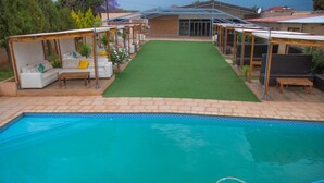 A swimming pool with a tiled edge, surrounded by a patio area with outdoor seating and a lawn. - ZAI OAT HOTEL (Makhuduthamaga)