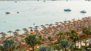 A beach resort with rows of sun umbrellas and lounge chairs, a marina with boats, and a view of the coastline. - Makadi Family Star Hotel (Makadi Bay)