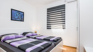 Un dormitorio moderno con una cama, una obra de arte en la pared, una ventana con persianas y suelo de madera.