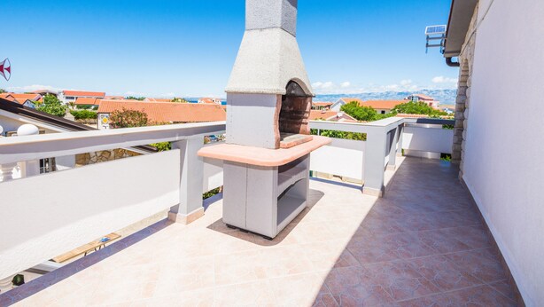 Una azotea con un horno de piedra al aire libre, una terraza con mesa y sillas, y vistas a edificios y montañas al fondo.