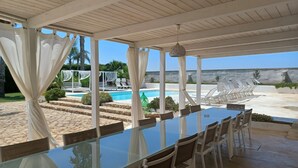Un espace extérieur abrité comprenant une piscine, des chaises longues et une table à manger avec des chaises.