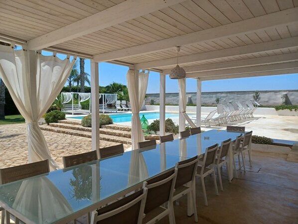 Un espacio al aire libre cubierto con piscina, sillas de descanso y una mesa de comedor con sillas.