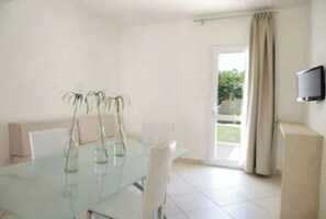 Un comedor moderno con una mesa de vidrio, sillas blancas y un televisor en la pared.