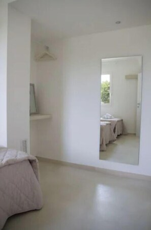 Habitación minimalista con un espejo grande, una cama y una pequeña mesa.