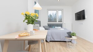 A modern bedroom with a bed, a desk with a laptop, a vase with flowers, and a TV on the wall. - Stylish Studio | Parking, close to Młociny Metro (Warszawa)