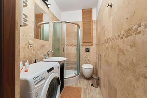 Een kleine badkamer met een wasmachine, wastafel, toilet en douchecabine.