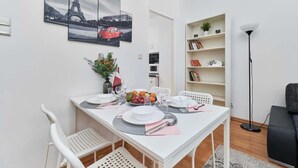 A dining area with a white table set for four, a bookshelf, and a floor lamp.