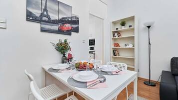 Ein Essbereich mit einem weißen Tisch, gedeckt für vier Personen, einem Bücherregal und einer Stehlampe.