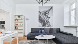 A modern living room with a black sectional sofa, a white coffee table, a patterned rug, and a large black-and-white Eiffel Tower artwork on the wall.