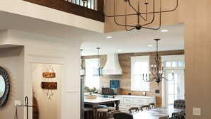 Een ruime woonkamer met een hoge plafond, een kroonluchter, een trap en uitzicht op de keuken.