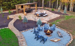 A patio area with stone flooring, outdoor furniture, a fire pit, and decorative trees.