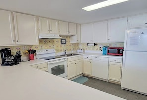 A kitchen with white cabinets, a microwave, a coffee maker, and a dishwasher. - Ocean Towers 101 (North Myrtle Beach)
