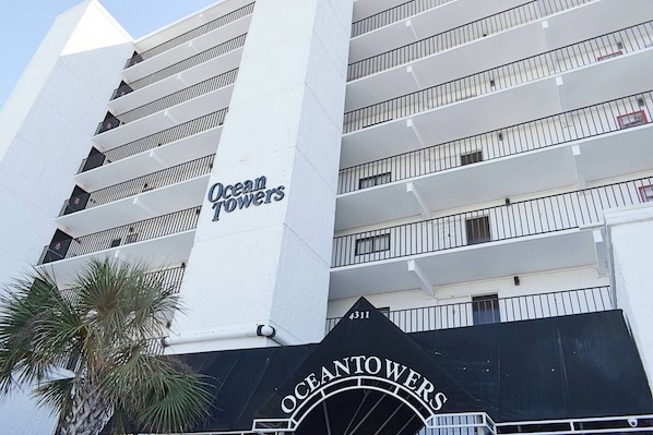 A multi-story hotel building named 'Ocean Towers' with balconies and a palm tree in the foreground.