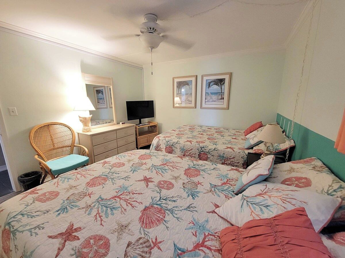 Een slaapkamer met twee bedden, een dressoir, een televisie en een plafondventilator.