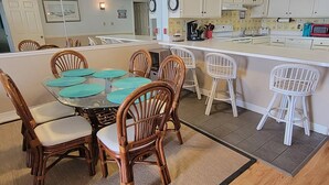 Un coin repas avec une table ronde et des chaises, une cuisine avec des meubles blancs et un petit îlot central avec des tabourets.
