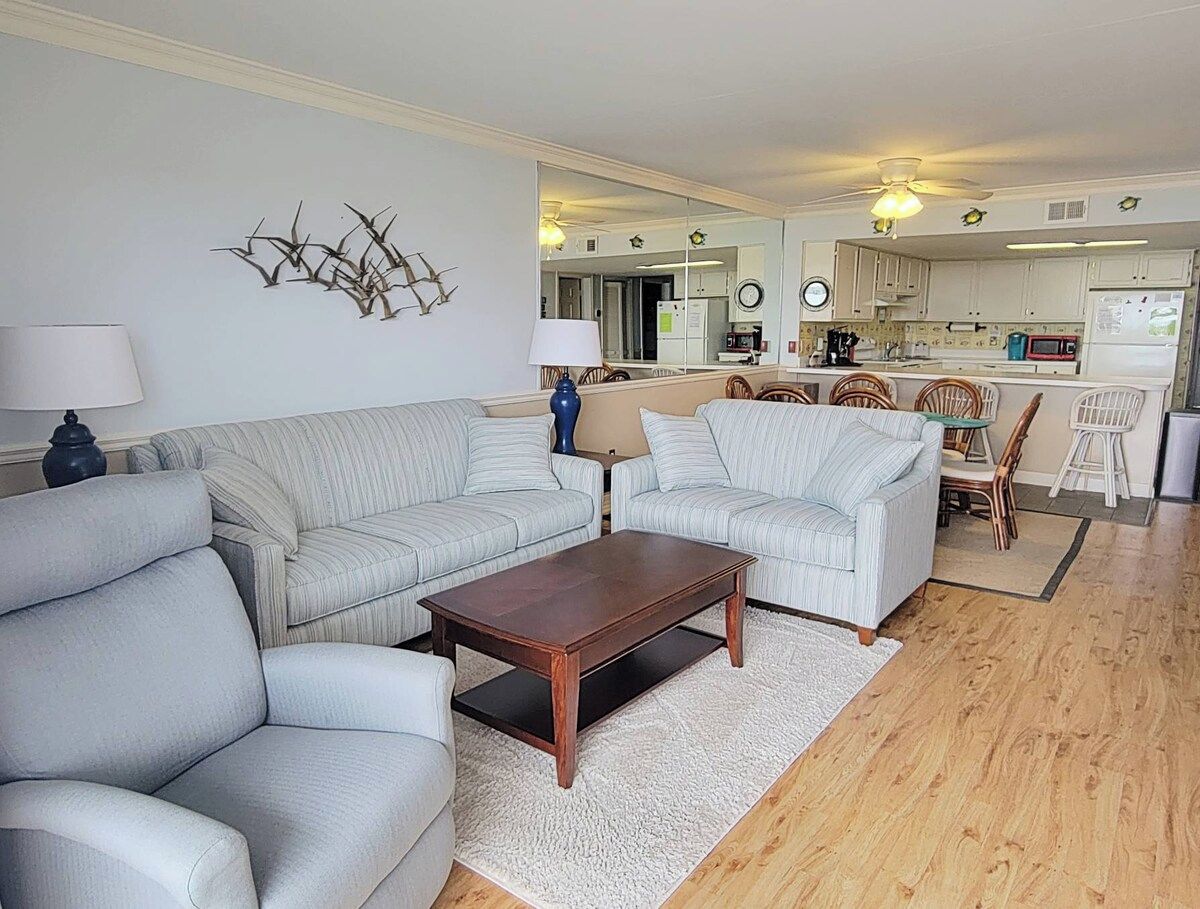 A living room with a sofa, a coffee table, and a dining area with chairs.