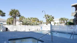 Un espace piscine avec un poste de surveillance pour les sauveteurs, une clôture blanche et des palmiers.