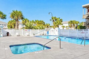 A swimming pool with a lifeguard stand, palm trees, and a white fence.