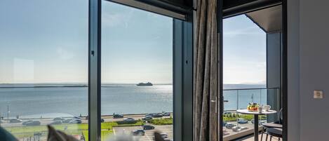 Een balkon met uitzicht op zee, een tafel met een kopje en een bord, en een stoel.
