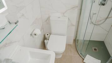 Un baño con inodoro, bidé y ducha con mampara de cristal.