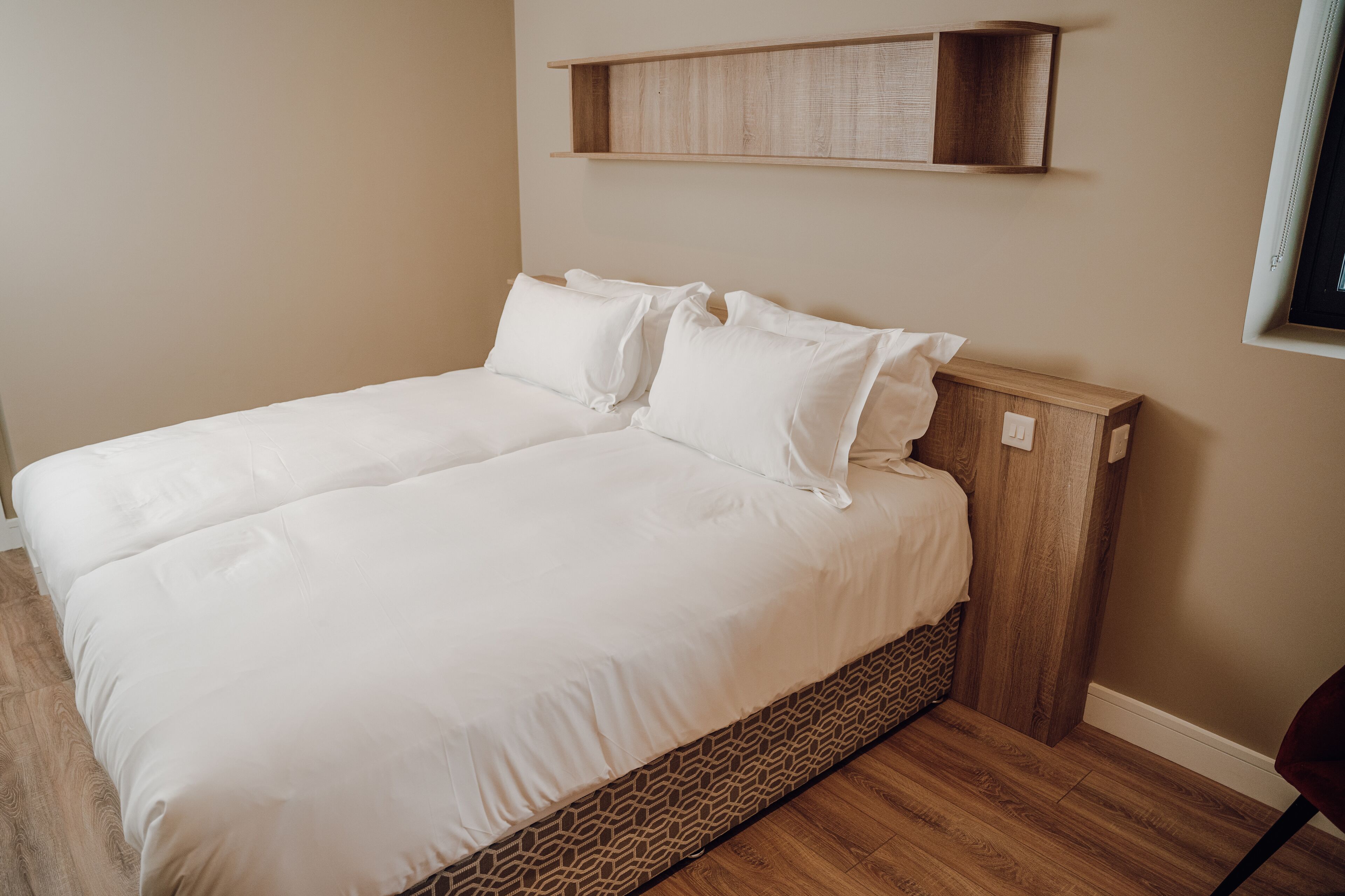 Una cama doble con ropa de cama blanca, un cabecero de madera y un almacenamiento integrado debajo.
