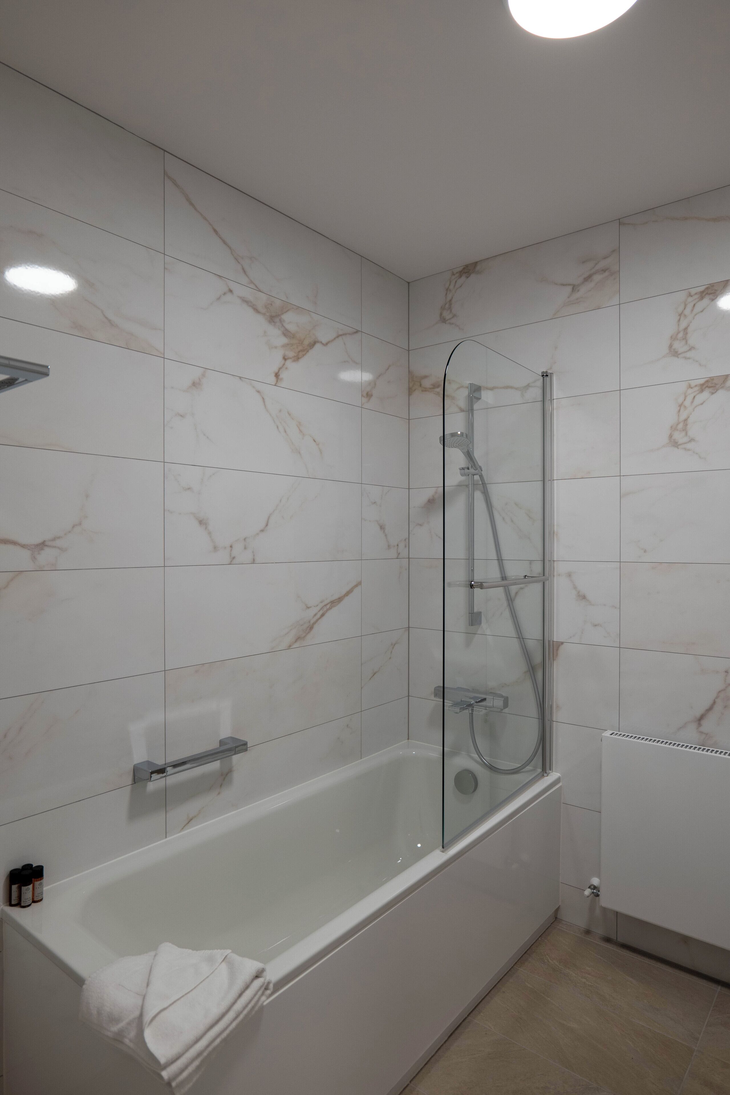 Un baño moderno con ducha envuelta en vidrio, una bañera blanca y paredes con diseño de mármol.